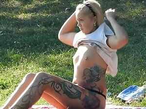 Cute blonde with wild tattoos relaxes in park